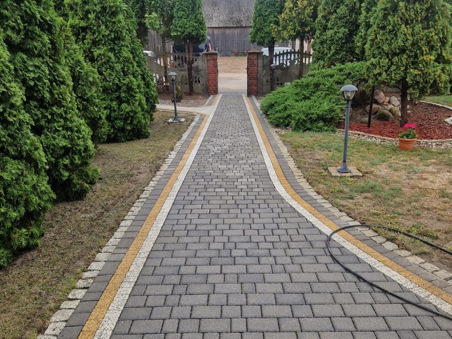 Długi podjazd z kostki brukowej obsadzony tujami po myciu